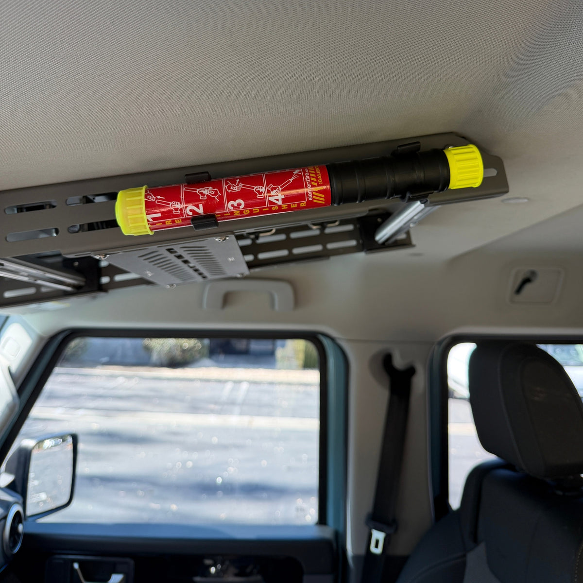 Element E50 fire extinguisher mounted in two Nylon 12 clips along the Cabdok in an Ineos Grenadier, seen from the drivers seat looking towards passenger seat