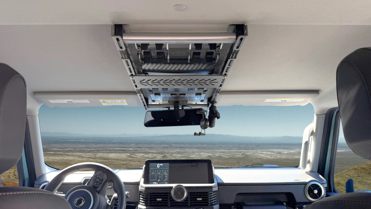 Cabdok overhead storage rack mounted in an Ineos Grenadier, with device pockets above the windshield and rearview mirror.