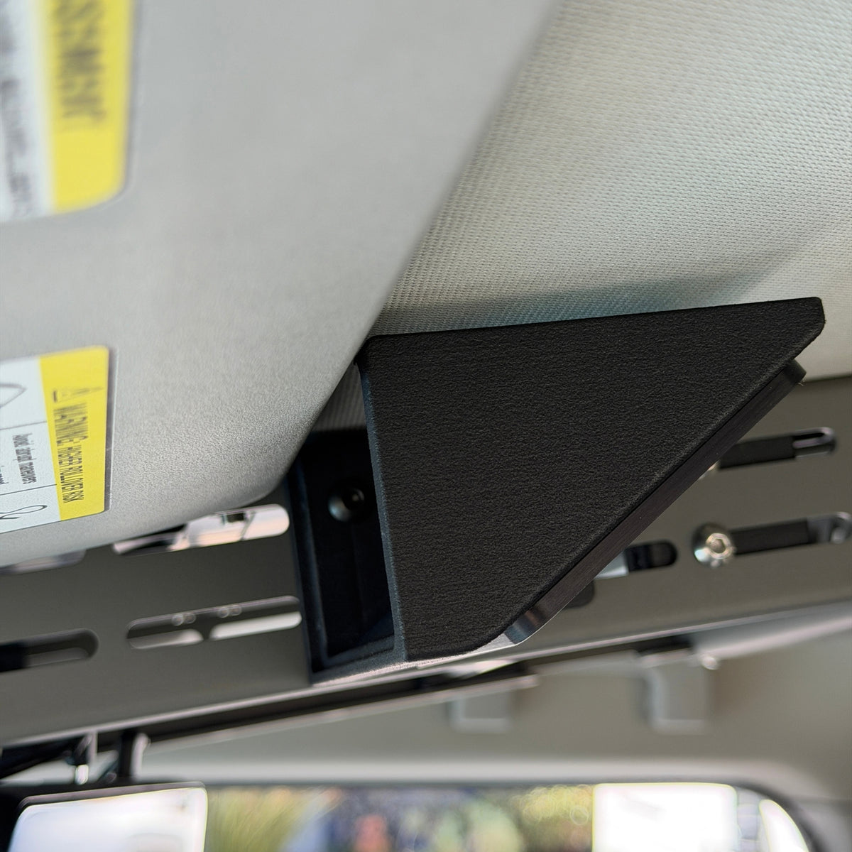 Black Nylon 12 Cabdok Switch-Pros Mount on the driver's side of the Cabdok in an Ineos Grenadier, seen from below next to the sun visor