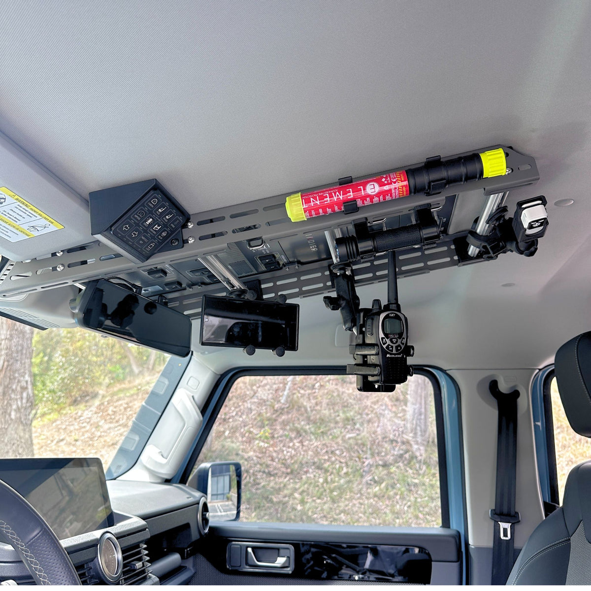 Cabdok overhead storage mount in Ineos Grenadier loaded with gear, including fire extinguisher, radio, and dash camera mount