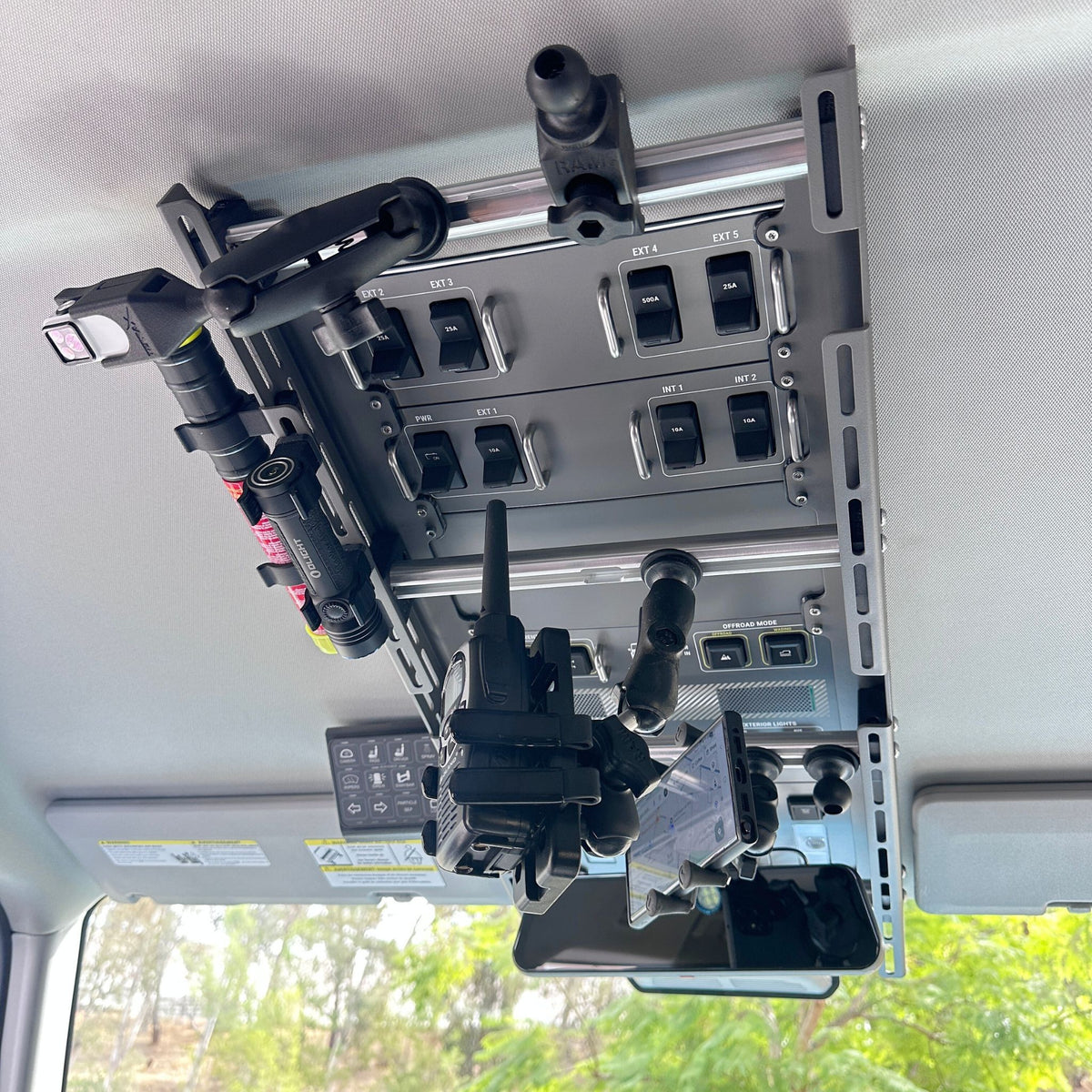 Cabdok overhead storage mount in Ineos Grenadier viewed from below, holding phone mount, radio, and flashlight