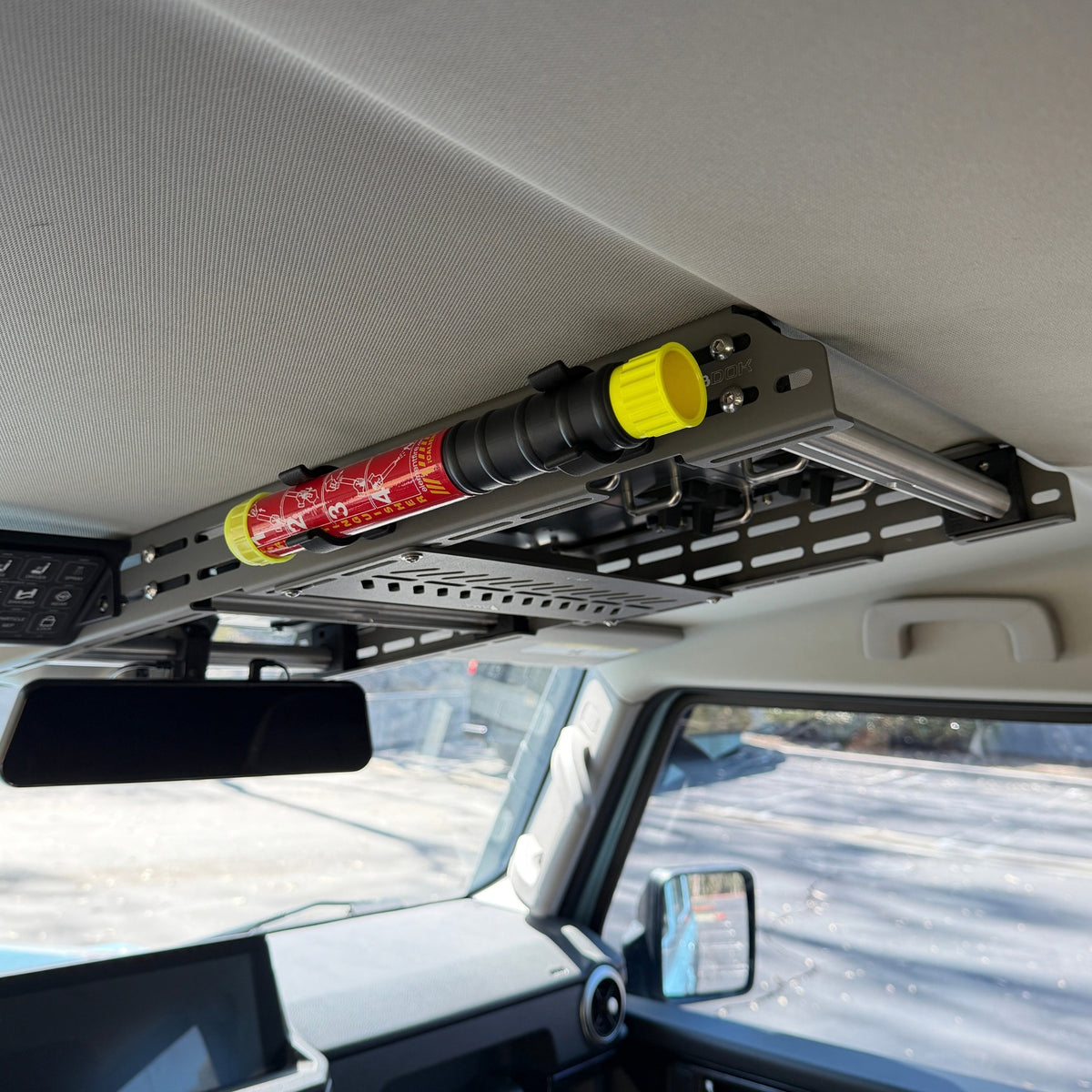 Element E50 fire extinguisher held in two black Nylon 12 clips on the side of the Cabdok in an Ineos Grenadier, seen from the front seat looking toward the rear