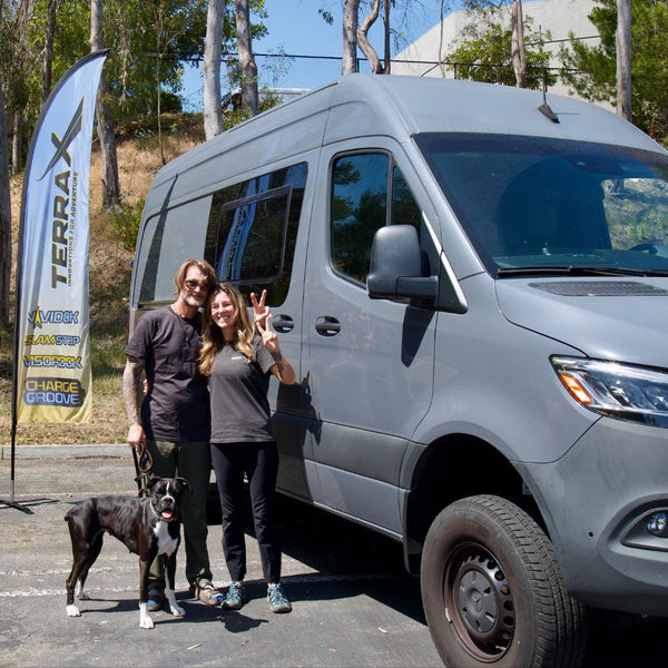 Jenny and Alex smiling with their dog Bliss in front of their van at the Terra X headquarters.
